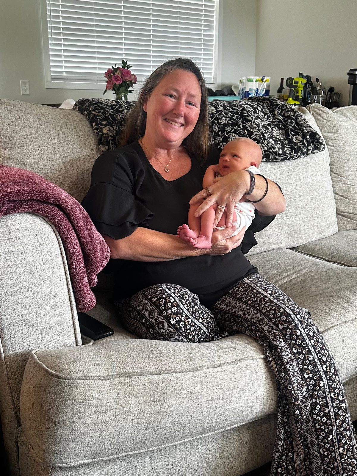 Kristie on a family’s couch at home, smiling as she holds baby Sarah Jane