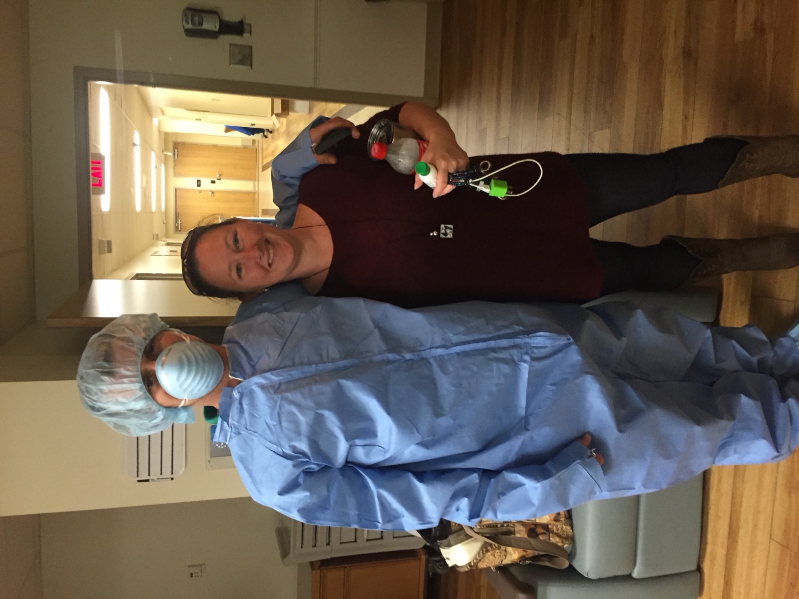 Kristie with a dad in a hospital gown, cap and mask, in a hospital hallway